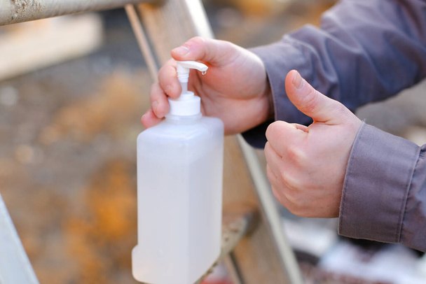 Sluiten bouwer desinfecterende handen met desinfectiemiddel op bouwplaats. - Foto, afbeelding