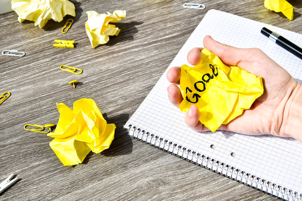 notebook e caneta em uma mesa de madeira, espaço de cópia para texto, escrita feminina GOAL em papel amarelo amassado, local de trabalho, brainstorming
 - Foto, Imagem