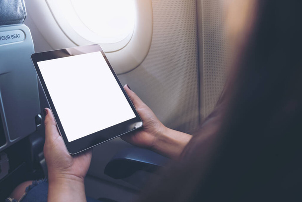 Mockup image of a woman holding and looking at black tablet pc with blank white desktop screen next to an airplane window with clouds and sky background - Fotó, kép