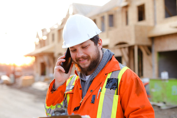 Portret van een voorman die met een smartphone praat op de bouwplaats. - Foto, afbeelding