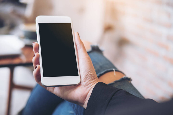Obrázek ženské ruky držící bílý mobilní telefon s prázdnou černou obrazovkou na stehně v kavárně - Fotografie, Obrázek