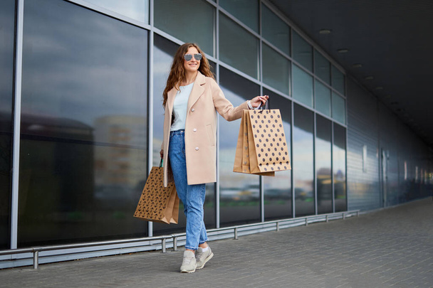 Femme avec des sacs à provisions sortant du magasin. Une fille commerçante dans des lunettes de soleil portant des sacs à provisions en plein air
. - Photo, image