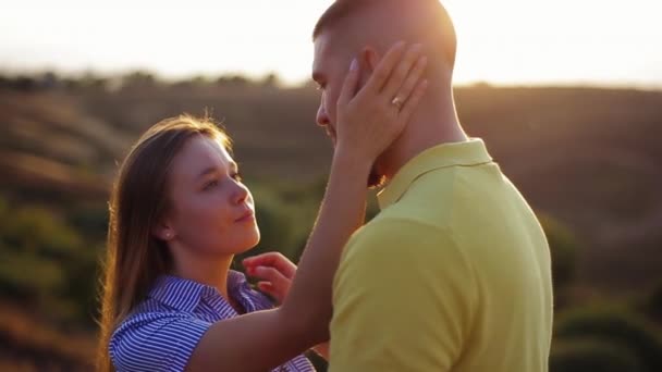 Close-up view of beautiful european girl with loving gaze stroking face of bearded guy, hugging leaning against him on blurry sunset background in slow motion. Romantic date of young couple at sunrise - Footage, Video