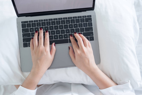 Top view close-up beeld van de handen van de vrouw typen op laptop op het bed in de slaapkamer - Foto, afbeelding