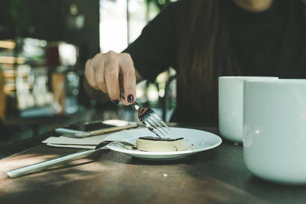 Imagen de cerca de una mujer cortando una galleta con tenedor en un plato blanco en una mesa de madera en un café
 - Foto, imagen