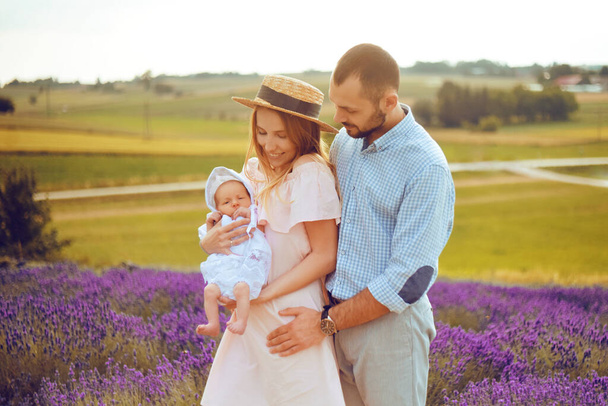Familia joven con un bebé en un fondo de campo de lavanda, viaje a Provenza. Hermosa rubia junto a su marido sosteniendo a un bebé en sus brazos. Familia joven feliz
. - Foto, Imagen