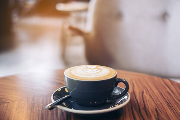 Detailní záběr na modrý šálek horké kávy latte s latte art na starožitném dřevěném stole v kavárně - Fotografie, Obrázek