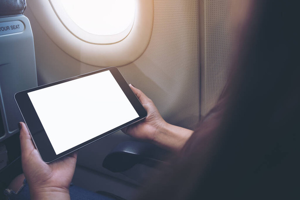 Mockup image of a woman holding and looking at black tablet pc with blank white desktop screen next to an airplane window - Photo, Image