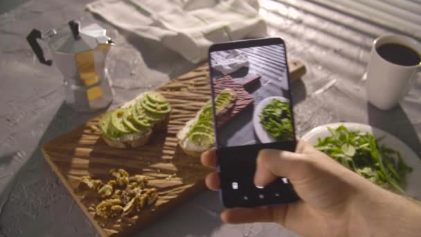 Zdravý stravovací koncept. Ruční fotografování sendvič s avokádem s chytrým telefonem - Záběry, video