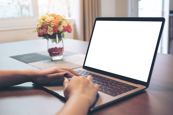 Макетне зображення рук жінки, що використовують і друкують на ноутбуці з порожнім білим екраном робочого столу на дерев'яному столі в будинку
 - Фото, зображення