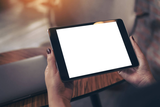 Imagen burlona de las manos de la mujer sosteniendo PC tableta negro con pantalla de escritorio blanco en blanco en la cafetería
  - Foto, Imagen