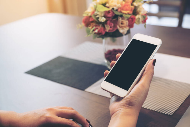 Imagem Mockup de mãos segurando smartphone branco com tela de desktop preta em branco e laptop na mesa de madeira
  - Foto, Imagem