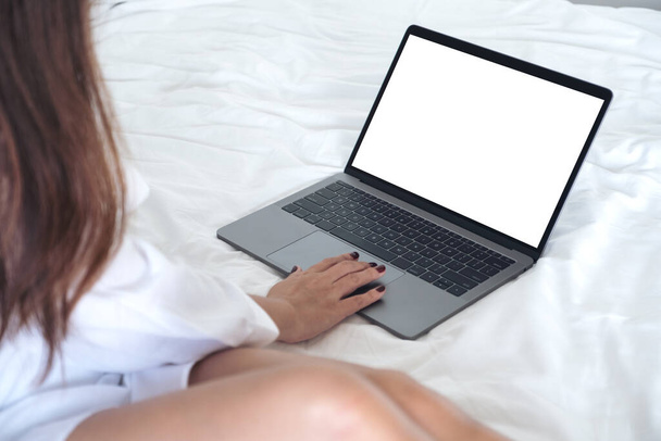 Mockup kép egy ázsiai nő ül az ágyon, használja és megérinti a laptop üres fehér asztali képernyő billentyűzet - Fotó, kép