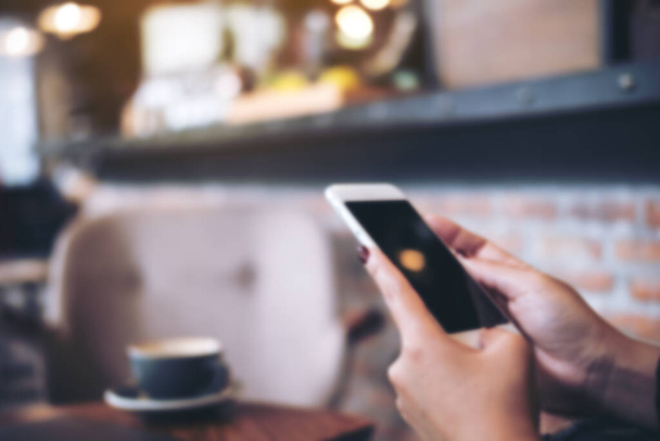 Image floue d'une femme tenant et utilisant un téléphone intelligent dans un café moderne - Photo, image