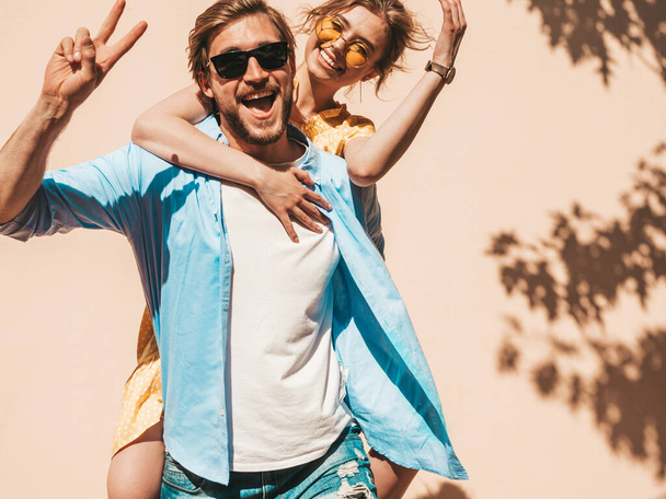 Portrait of smiling beautiful girl and her handsome boyfriend. Woman in casual summer dress and man in jeans. Happy cheerful family. Female having fun in the street near wall - Foto, Bild