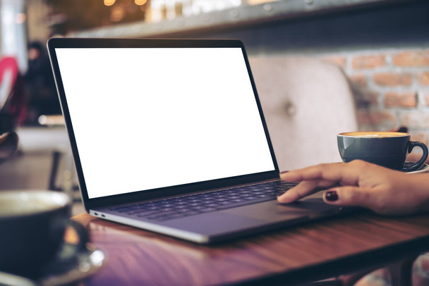 Mockup image of a businesswoman using laptop with blank white desktop screen with coffee cup on wooden table in cafe - Photo, Image