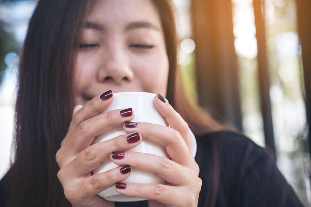 Imagen de cerca de una hermosa mujer asiática sosteniendo una taza blanca de café caliente con sentirse feliz en la cafetería - Foto, Imagen