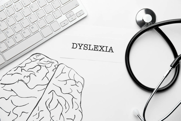 Πληκτρολόγιο υπολογιστή, σχεδιασμένος εγκέφαλος, στηθοσκόπιο και λέξη DYSLEXIA σε λευκό φόντο - Φωτογραφία, εικόνα