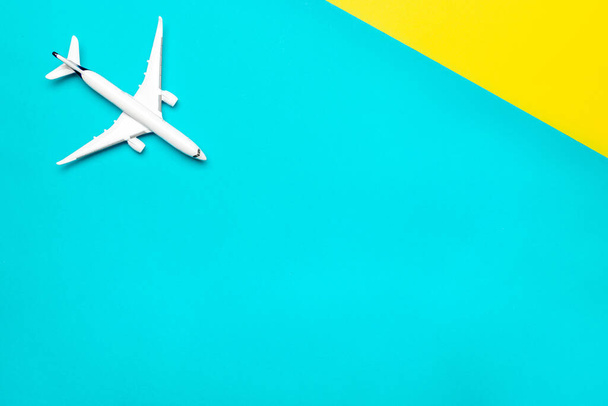 Travel background. White toy airplane, aircraft on bright blue and yellow backdrop. Flight or fly in sky air plane concept. - Photo, Image