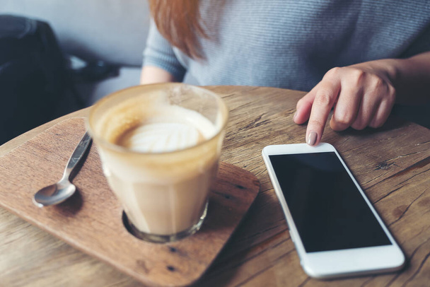 Immagine da primo piano della mano di una donna che punta il dito verso uno smartphone con una tazza di caffè sul tavolo di legno nel caffè - Foto, immagini