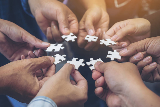 Closeup image of many people hands holding a jigsaw puzzle in circle together - Photo, Image