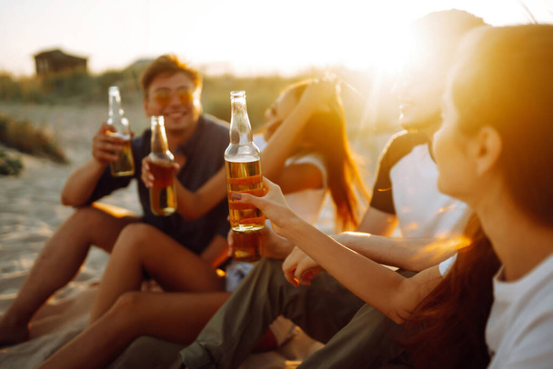 Young people sitting together at beach, drinking beer and having a party. Group of friends cheers with beers at the beach during summer vacation. - Фото, зображення
