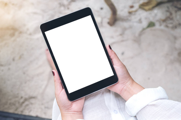 Immagine mockup della mano di una donna che tiene il tablet PC nero con schermo desktop bianco vuoto con sabbia e sfondo della spiaggia - Foto, immagini