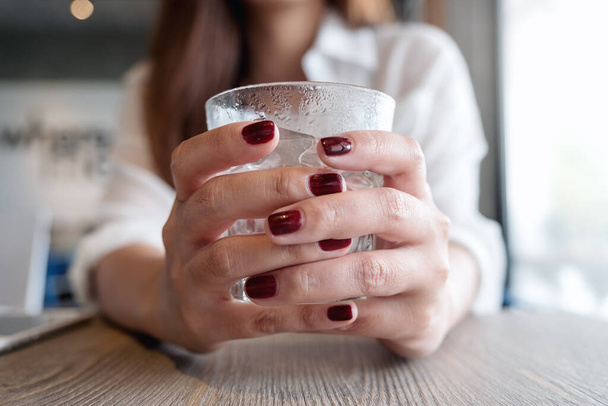 Closeup image of woman's hands with red nails color holding a glass of cold water  - Fotoğraf, Görsel