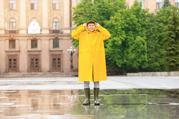 Jovem asiático de capa de chuva na rua da cidade
 - Foto, Imagem