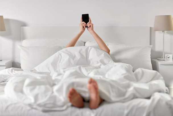hands of woman lying in bed with smartphone - Foto, imagen