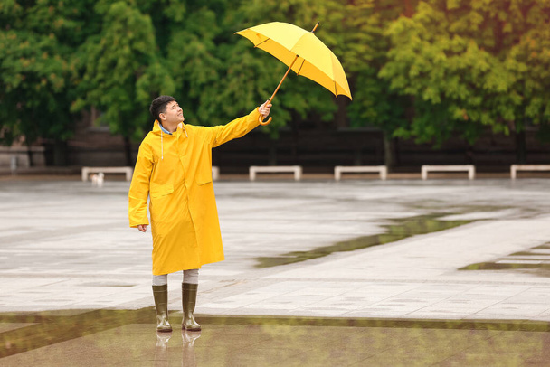 Νεαρός Ασιάτης με αδιάβροχο και ομπρέλα στο δρόμο της πόλης - Φωτογραφία, εικόνα
