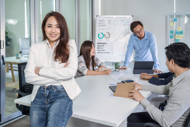 Portrait einer asiatischen Geschäftsfrau mit überkreuzten Armen und über der Gruppe ihres Kollegen stehend beim Brainstorming-Meeting am modernen Arbeitsplatz, Personal- und Kleinunternehmenskonzept - Foto, Bild