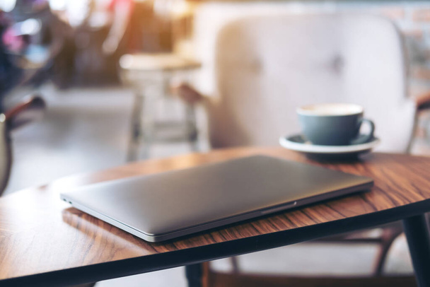 Lähikuva kuva hopea väri kannettava tietokone ja kahvi kuppi puinen pöytä hämärä kahvila tausta - Valokuva, kuva