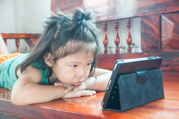 Нещаслива дівчина лежить на дерев'яному стільці і навчається онлайн курсу на Wireless Digital Tablet, перебуваючи вдома в ситуації Corona Virus або Covid 19 спалаху. - Фото, зображення