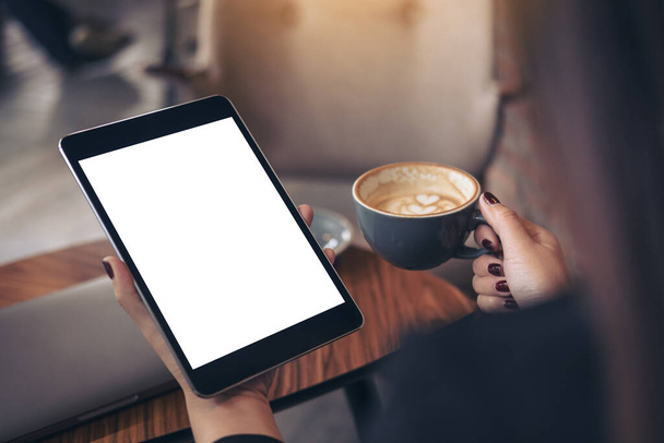 Mockup image of woman's hands holding black tablet pc with blank white desktop screen and coffee cup in cafe background - Foto, Imagen
