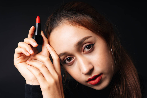 Close up portrait of pretty beautiful young woman wearing black sweater isolate over dark background. Beauty in the dark. Woman with cosmetic red lipstick on hand. - Φωτογραφία, εικόνα