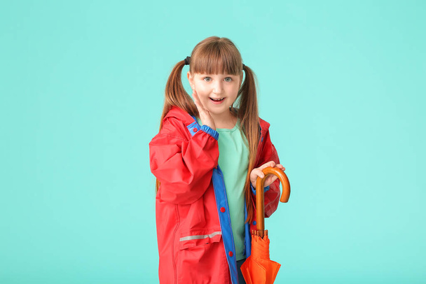 Cute little girl in raincoat and with umbrella on color background - Fotoğraf, Görsel