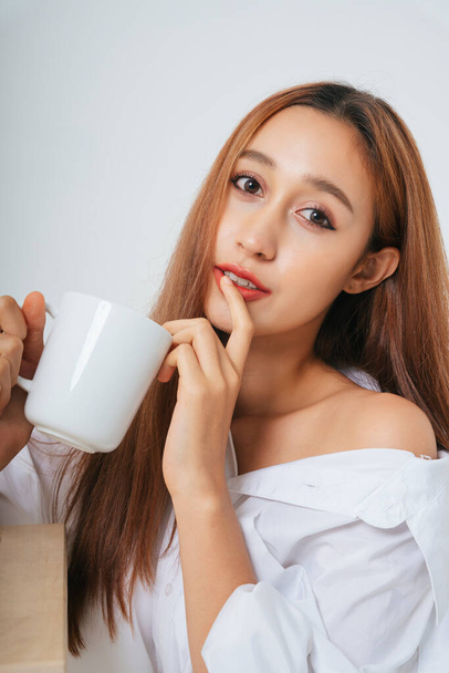 Beautiful woman in white shirt with natural make up isolated over white background. Skincare facial treatment. Woman drinking water coffee tea from white mug cup. Woman with a cup. - Фото, зображення