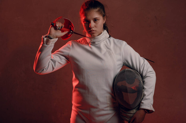 Fencer vrouw met hekwerk epee zwaard op schouder in rood licht - Foto, afbeelding