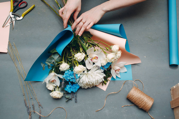 Çiçekçi, gri masa manzaralı butikte buket yapar.. - Fotoğraf, Görsel