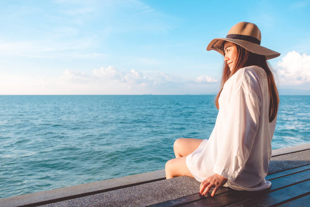 青い空を背景に海のそばに木製のバルコニーに座って白いドレスに幸せなアジアの女性の肖像画 - 写真・画像