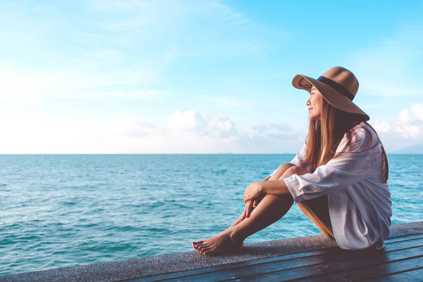 Retrato imagen de una hermosa mujer asiática feliz en vestido blanco sentado en balcón de madera junto al mar con fondo de cielo azul claro
 - Foto, Imagen