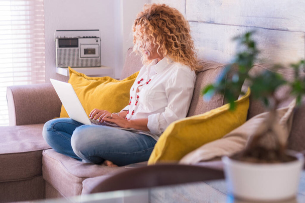 Yetişkin bir kadın bilgisayarlı dizüstü bilgisayarla çalışıyor. Kanepeye oturup teknolji ve iletişim cihazlarının keyfini çıkarıyor. Güzel insanlar video konferansında kadın. - Fotoğraf, Görsel