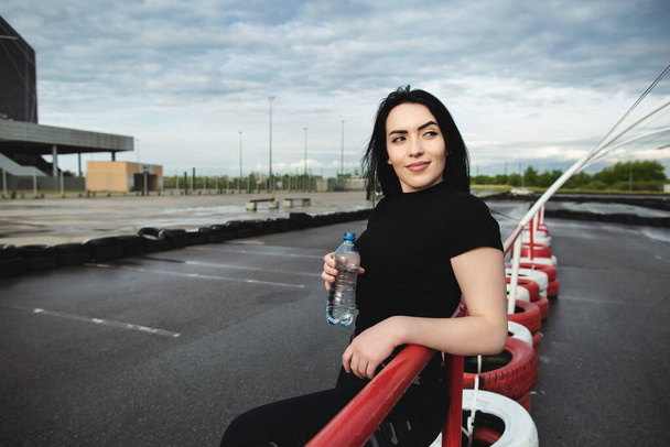 Красивая молодая женщина на спортивной площадке с бутылкой воды в руках
. - Фото, изображение