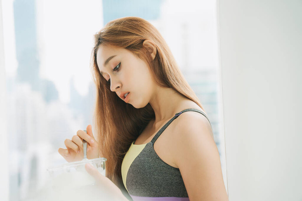 Side view of beautiful woman in sport bra enjoy eating tasty yogurt at home. Quarantine at home. - Foto, Imagen