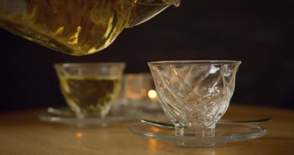 Közelről lőtték le. Teát önteni a teáskannából egy pohárba. Üveg teáskanna és csésze. A gőz forró teából származik. Zöld tea. 4K - Felvétel, videó