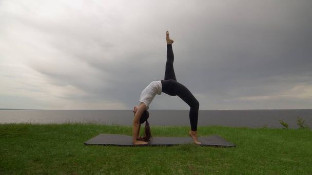 Giovane donna in forma pratica yoga sulla costa vicino al lago o al mare. Donna che fa Wheel Urdhva Dhanurasana posa
 - Foto, immagini