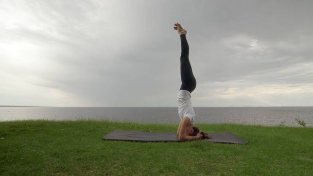 Молода жінка практикує йогу на узбережжі біля озера або моря. Жінка робить Підтримувані головні убори III Саламба Сірсана C Поза
 - Фото, зображення