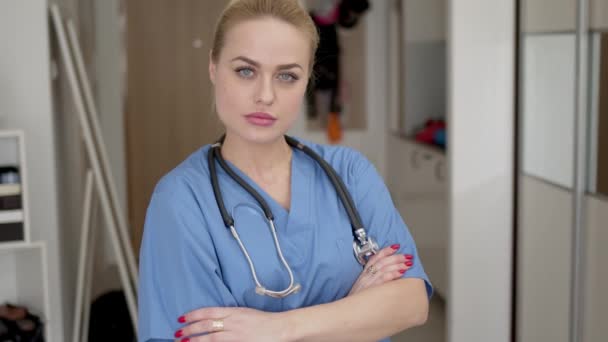Head shot of female doctor wearing blue coat and stethoscope on shoulders looking at camera - Filmmaterial, Video