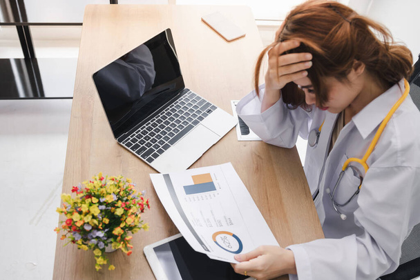 Stressed exhausted young Asian doctor with hands on face feeling depression at workplace in clinic. Covid-2019, Coronavirus epidemic disease, Health medicine protection. - Photo, image